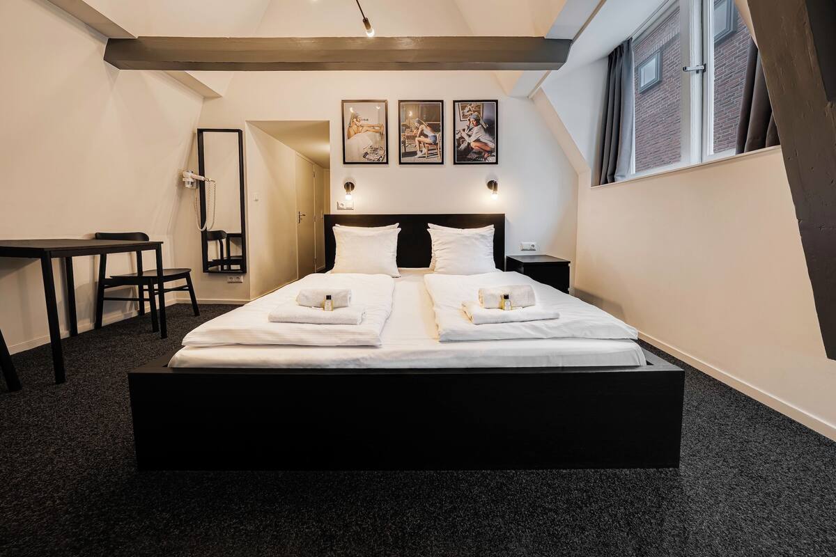 A hotel room with a large bed, a desk, a mirror, and three framed pictures on the wall.