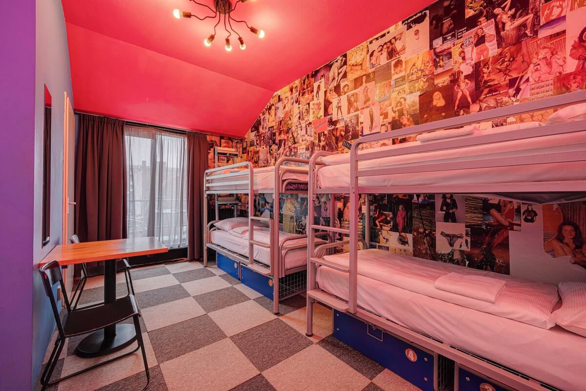 A room with bunk beds, a checkered floor, a table with a chair, and a wall covered with posters.