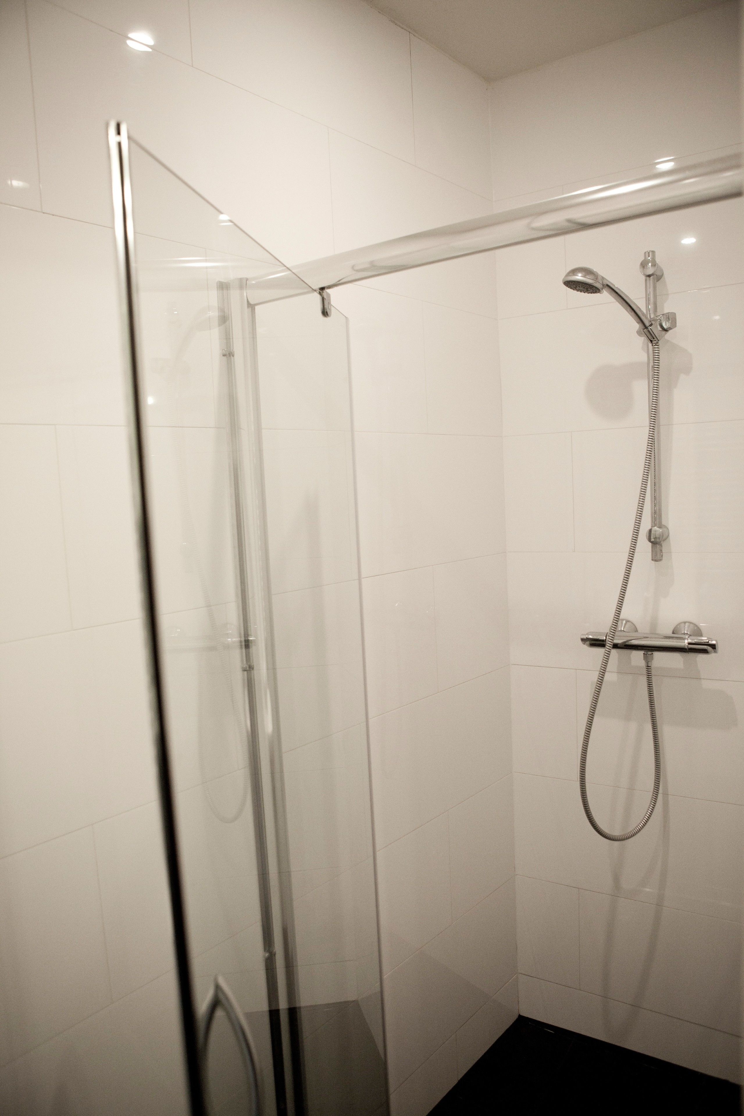 A glass-enclosed shower with a handheld showerhead and a wall-mounted faucet.