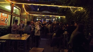 An outdoor dining area with tables and chairs, string lights, and a crowd of people. - St Christopher's at The Winston - Hostel (Amsterdam)