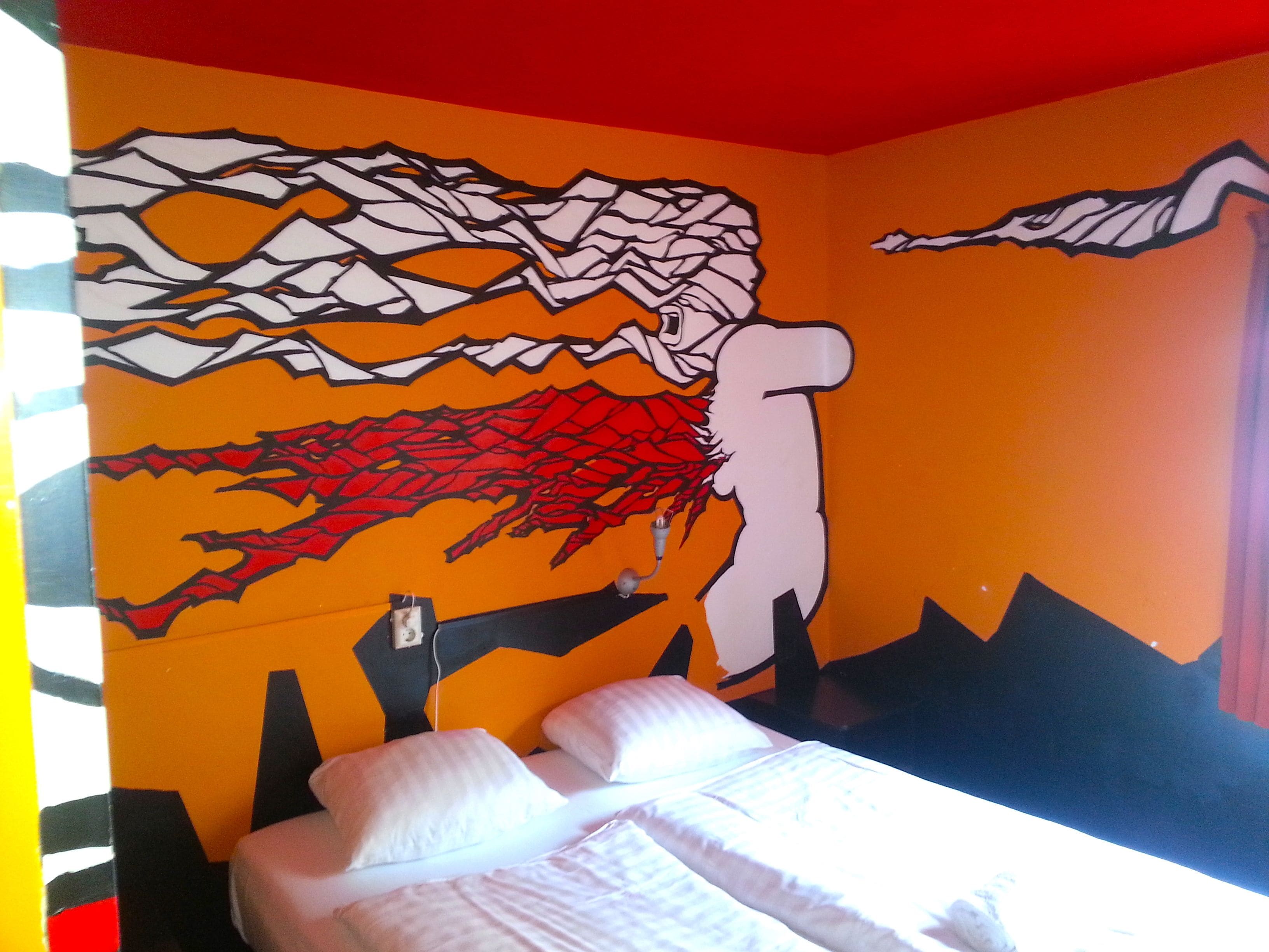 Een kamer met een bed, een muurschildering en een raam.