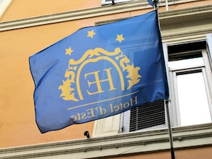 A blue flag with a golden emblem and the text "Hotel b' Este" on a building facade. - D'este (Rome)
