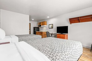 A hotel room with two beds, a desk with a computer, a television, and a kitchenette.