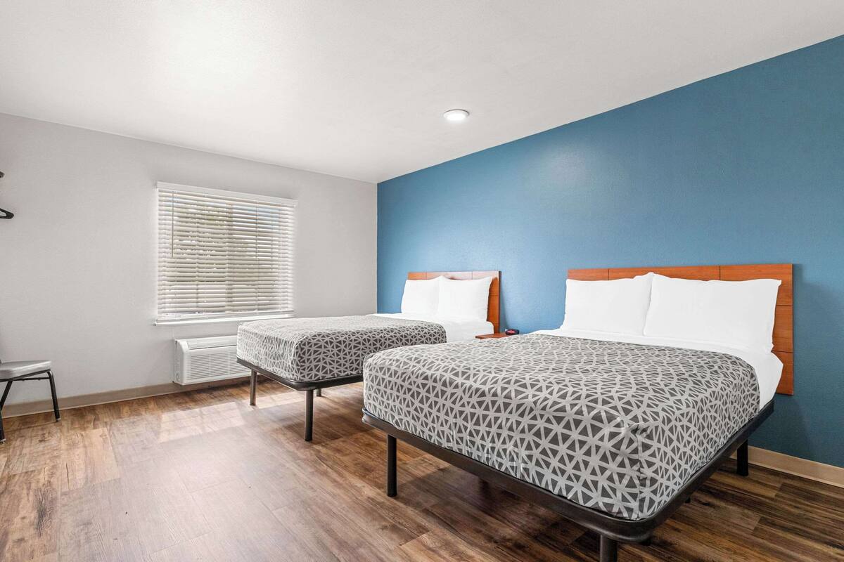 A room with two beds, a window with blinds, a radiator, and a chair.