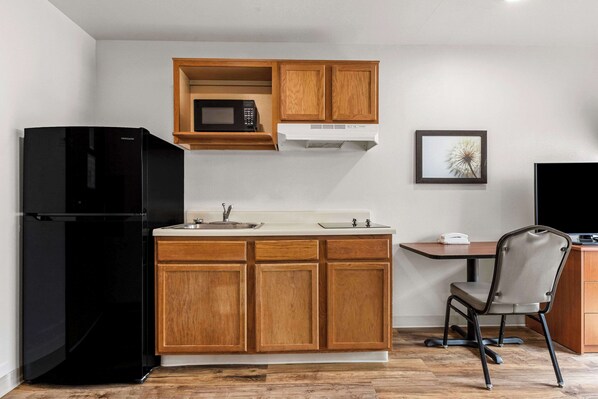 Cocina compacta con armarios de madera, refrigerador negro, microondas y un pequeño comedor con una silla.