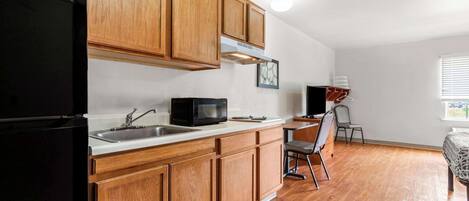 A kitchen with wooden cabinets, a black refrigerator, a microwave, and a sink.
