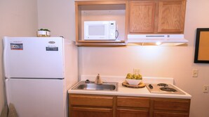 Une cuisine de taille réduite équipée d’un réfrigérateur, d’un four à micro-ondes, d’un évier et de meubles de rangement en bois.