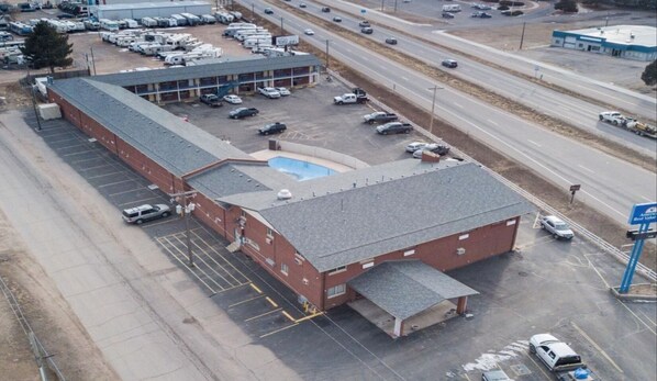 An aerial view of a multi-story building with a parking lot, a swimming pool, and a road with vehicles. - Americas Best Value Inn Greeley Evans (Evans)