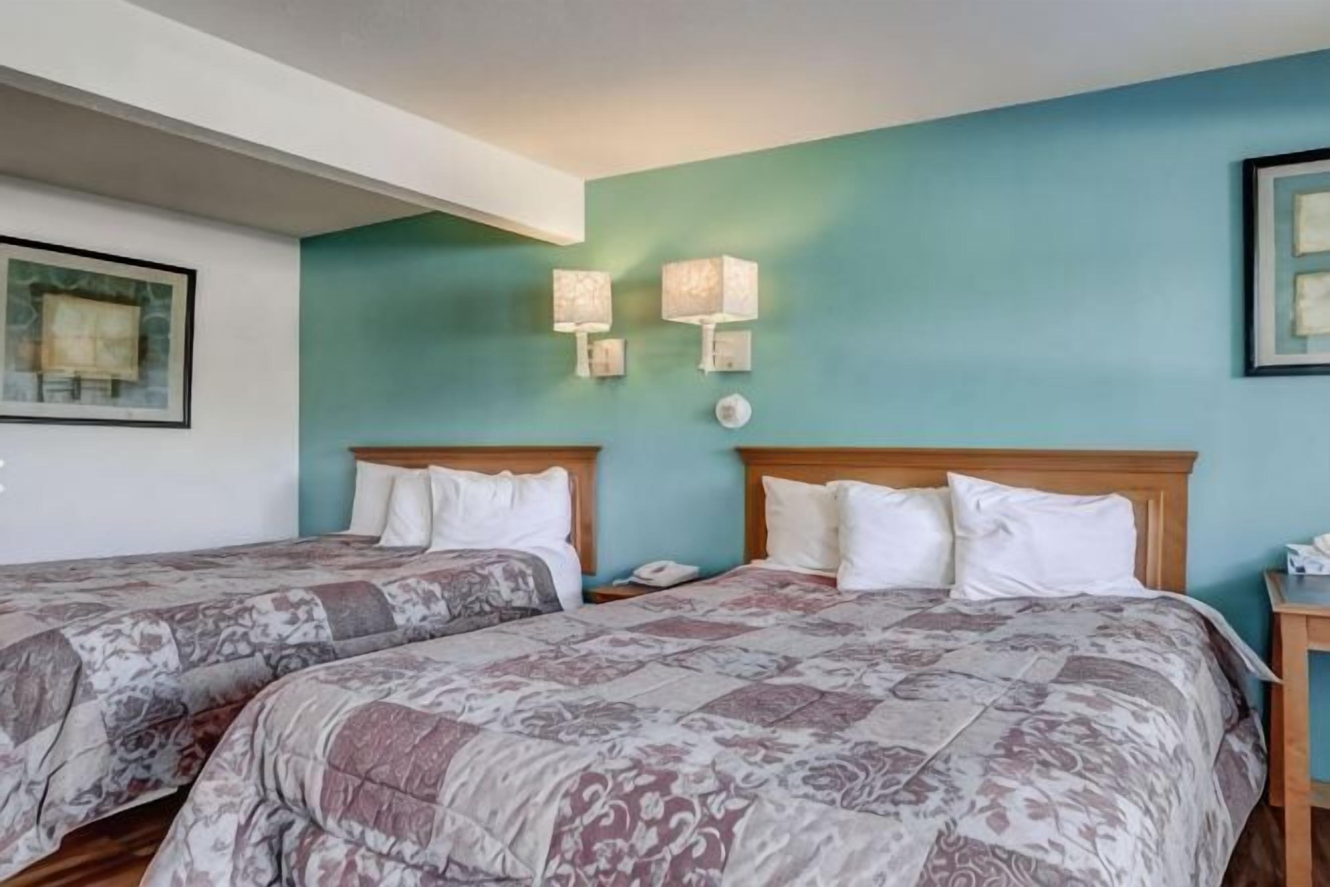 Een hotelkamer met twee bedden, een blauwgroene wand en twee wandlampen.