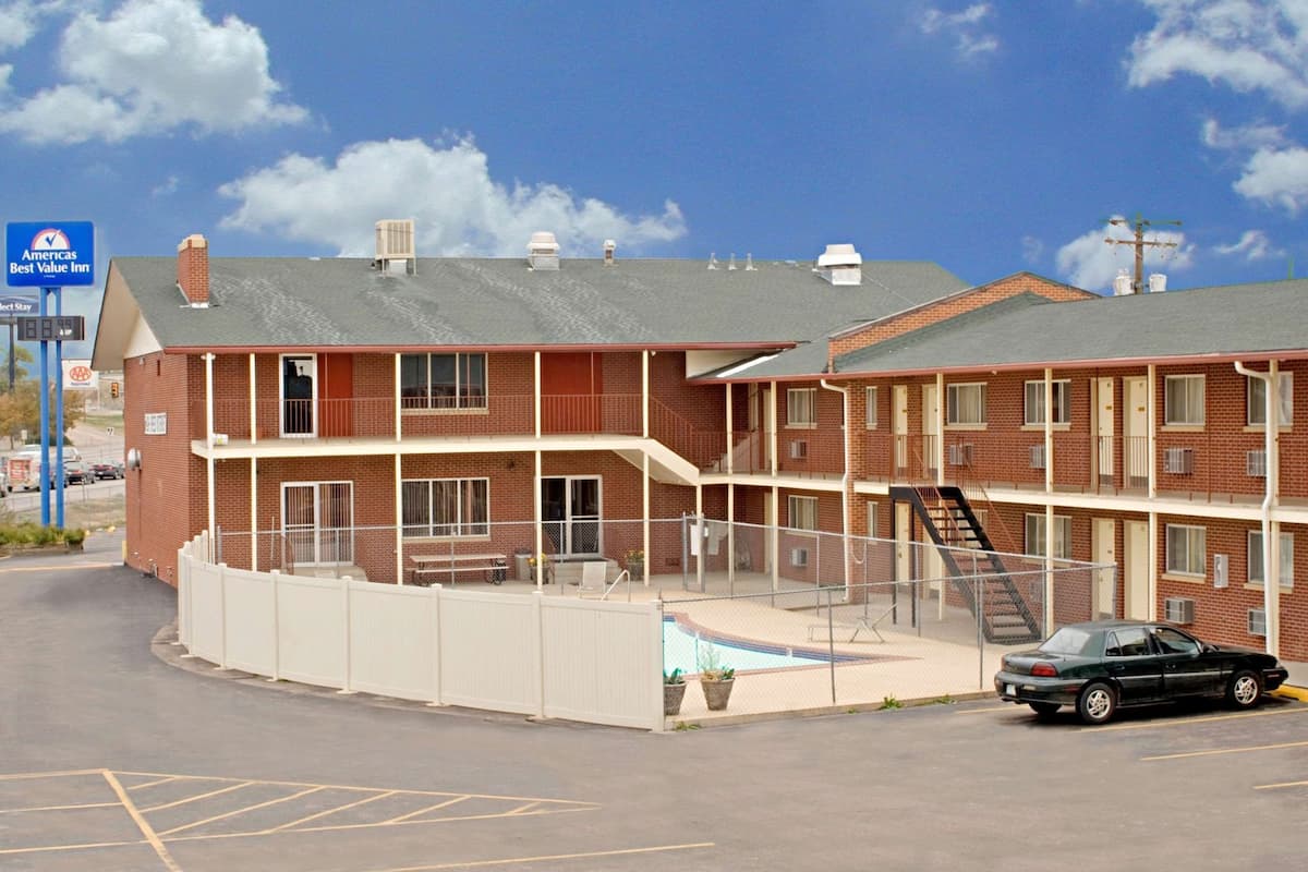 A multi-story motel with a fenced patio area, a car parked in front, and a clear sky.