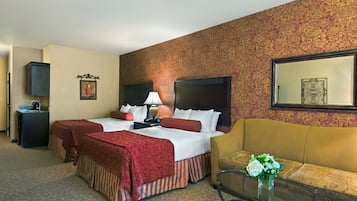 A hotel room with two beds, a sofa, a coffee table, and a TV.