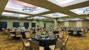A banquet hall with round tables set for events, featuring ceiling lights and a patterned carpet.