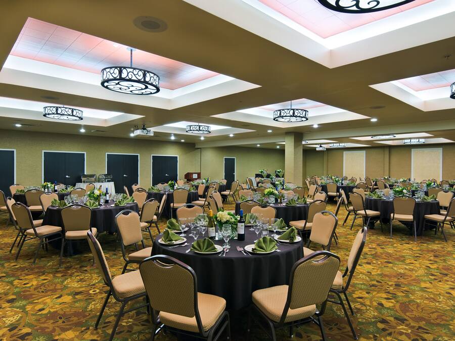 A banquet hall with round tables set for events, featuring ceiling lights and a patterned carpet.