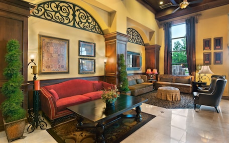 A spacious living room with a red sofa, a coffee table, and a patterned rug. There are two side tables with lamps, a large window with curtains, and a ceiling fan.