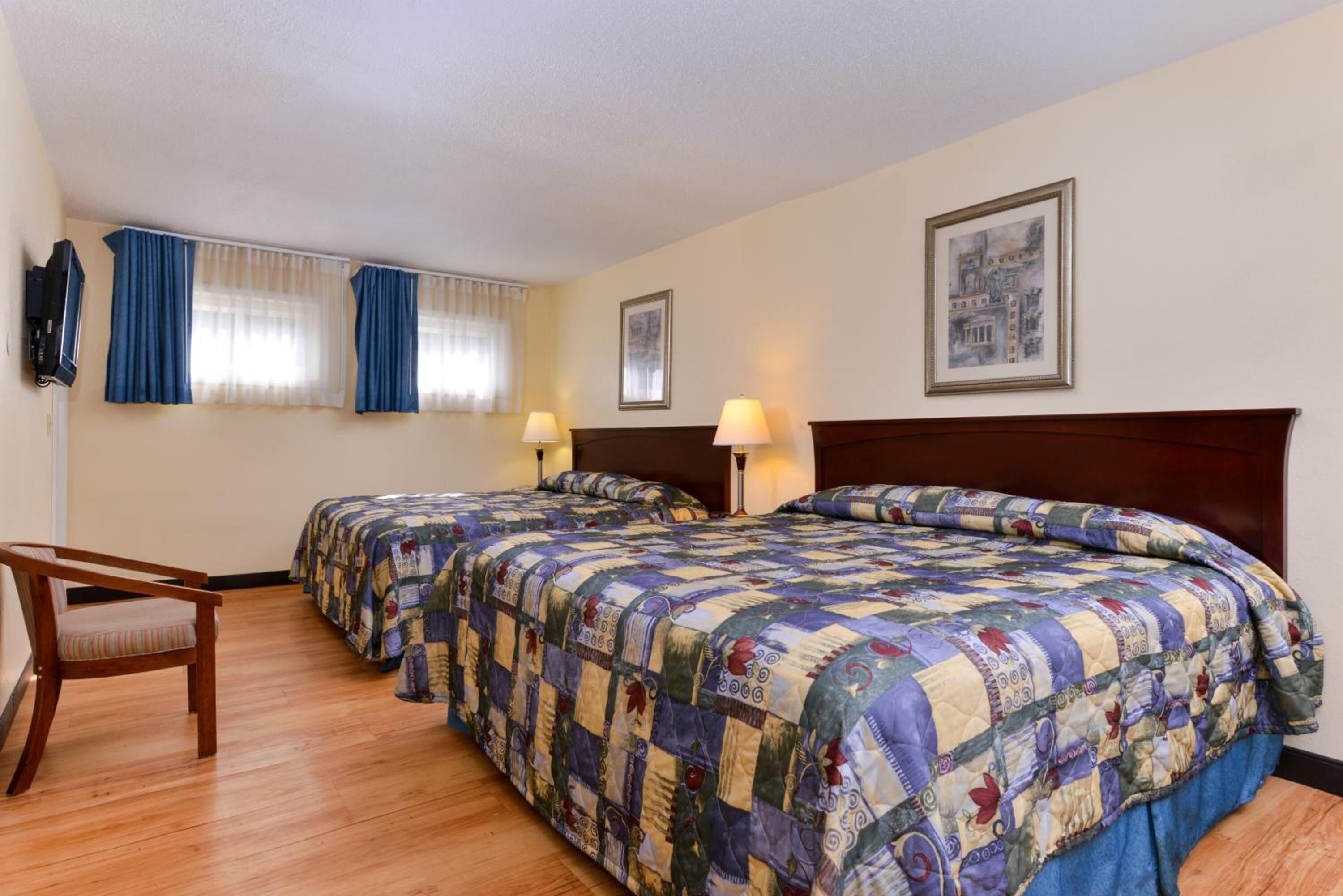 A hotel room with two beds, a desk, and a chair.