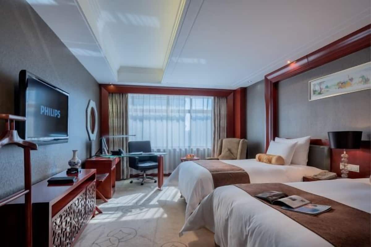 A hotel room with a television, two beds, a desk, a chair, and a window with curtains.