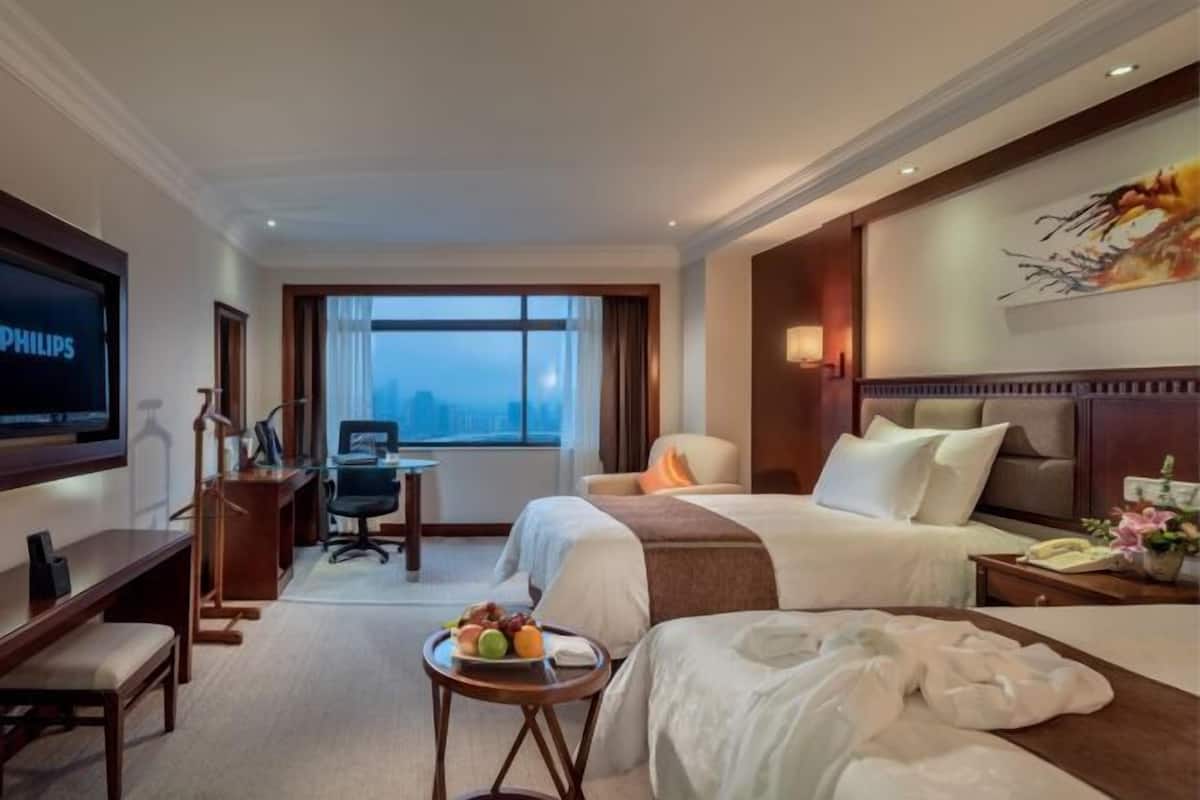 A hotel room with a bed, a desk, a chair, a TV, and a window with a view.