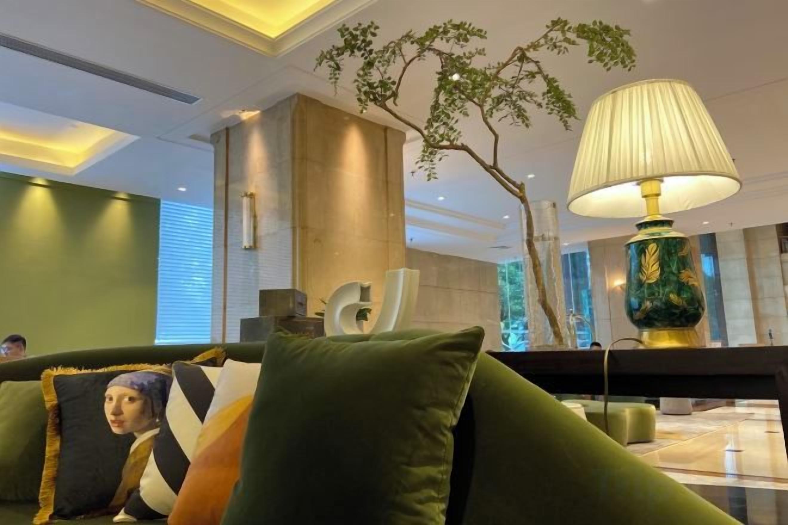 Un hall d’entrée moderne avec un canapé vert, une lampe décorative et une grande plante d’intérieur.