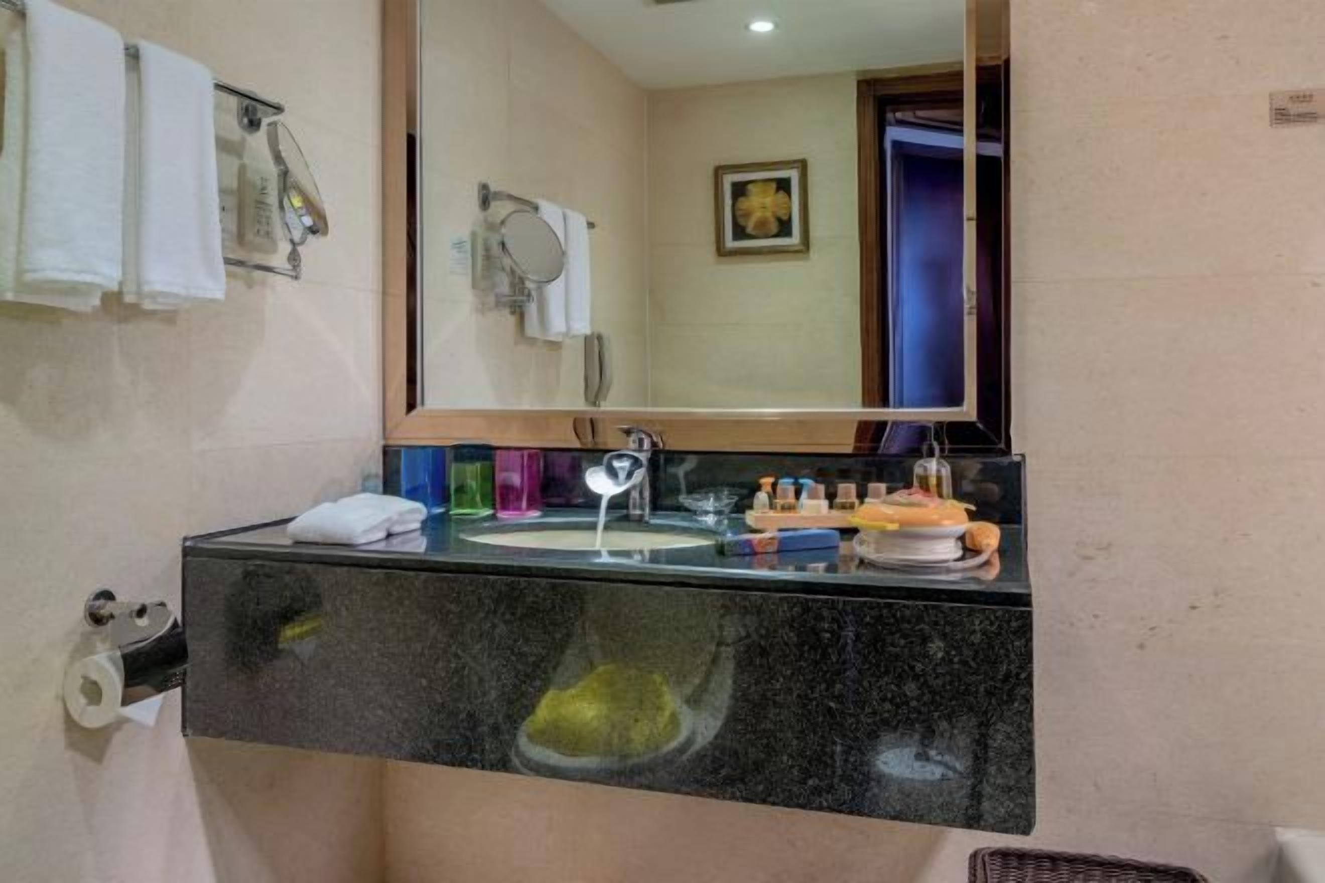 A bathroom with a black countertop, a mirror, a sink, and a towel rack.