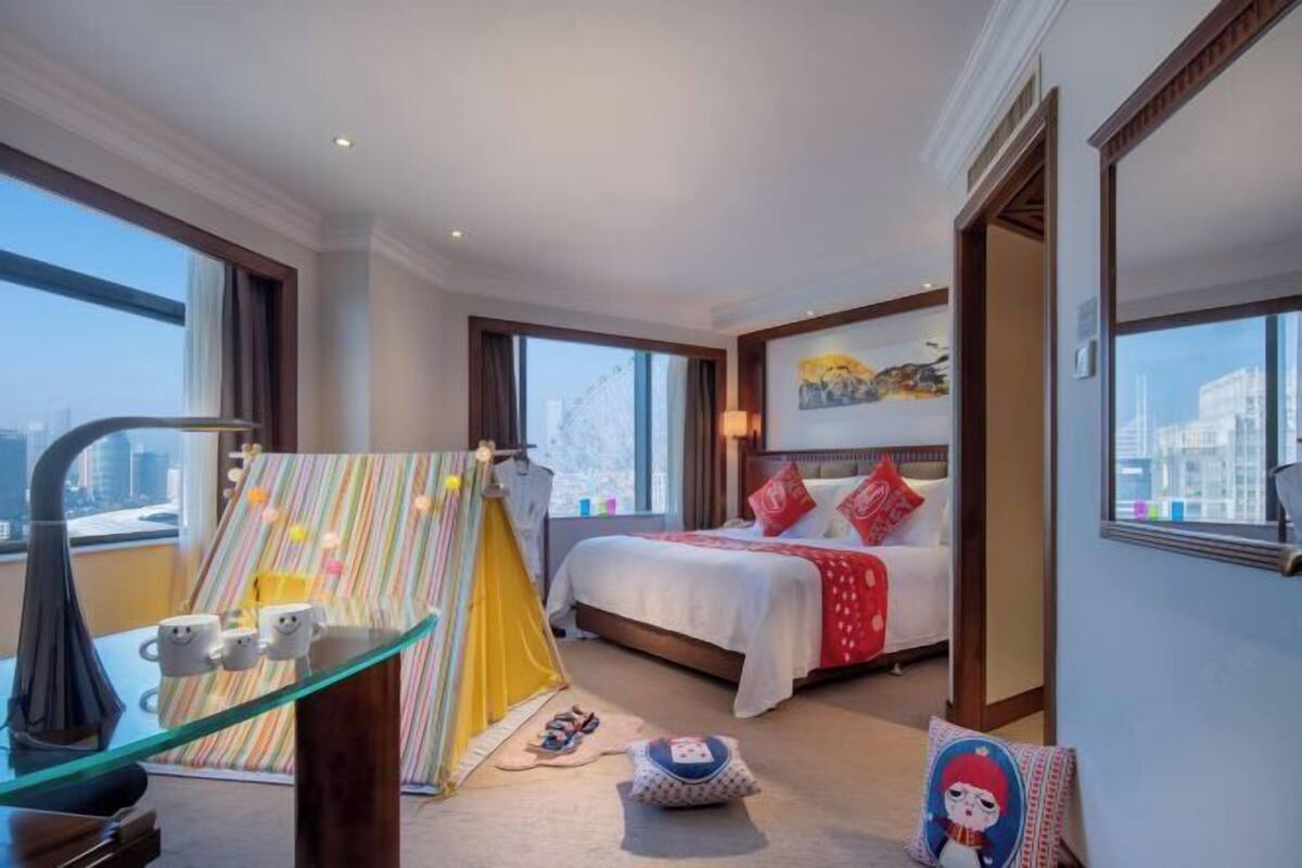 A hotel room with a bed, a desk with a lamp, a window, and a city view.