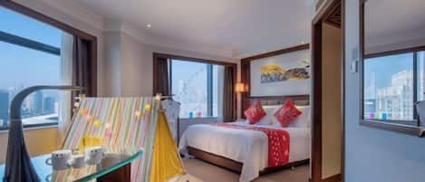 A hotel room with a bed, a desk with a lamp, a window, and a city view.