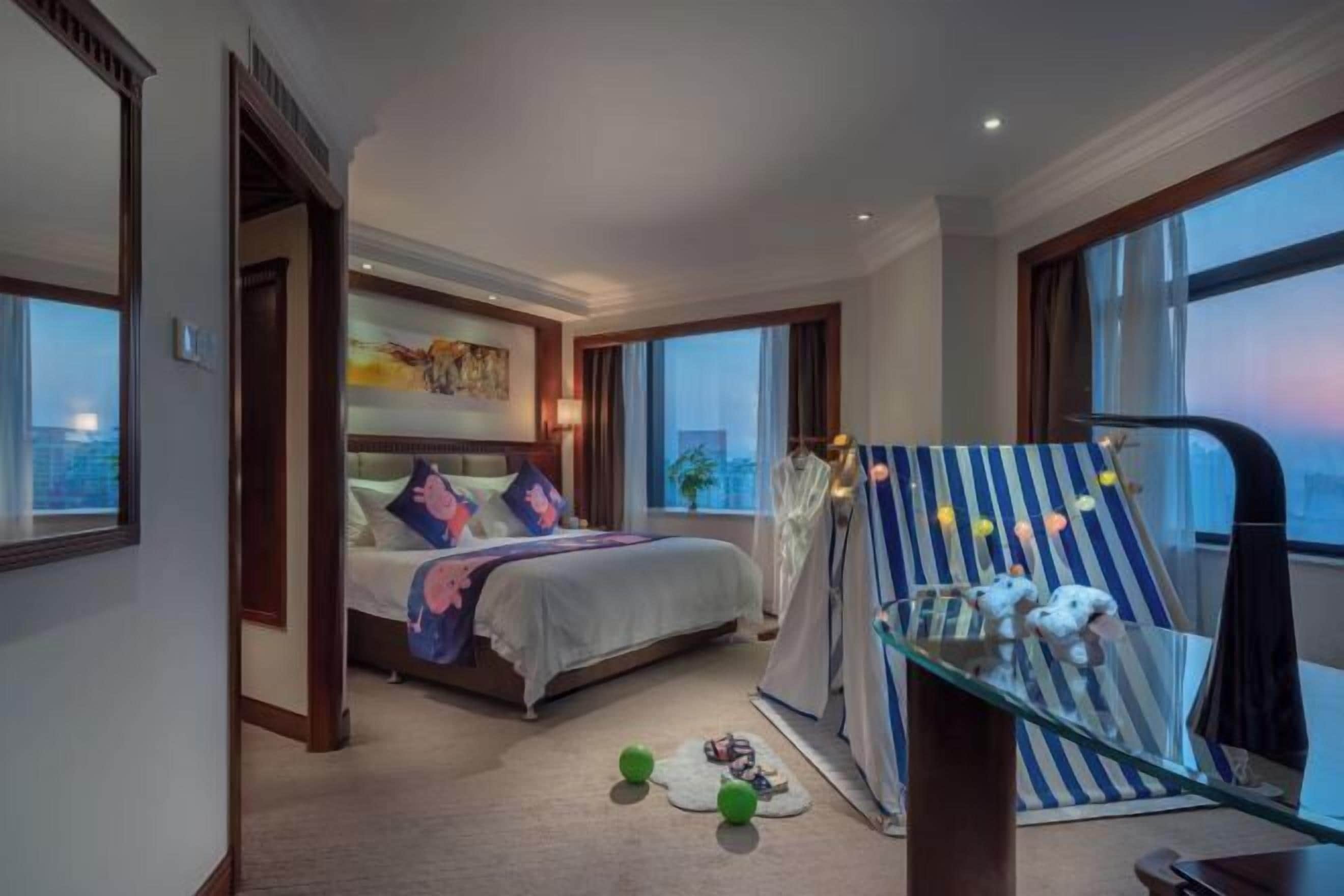 Habitación de hotel con cama, una mesita de vidrio con juguetes, vista a la ciudad y un ventanal grande.