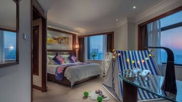 Habitación de hotel con cama, una mesita de vidrio con juguetes, vista a la ciudad y un ventanal grande.