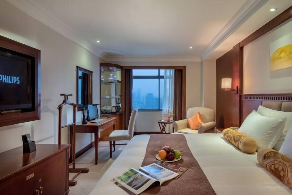 A hotel room with a bed, a desk with a computer, a television, and a view of the city.