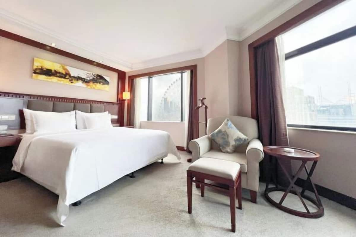 A hotel room with a large bed, a chair, a small table, and a painting on the wall.