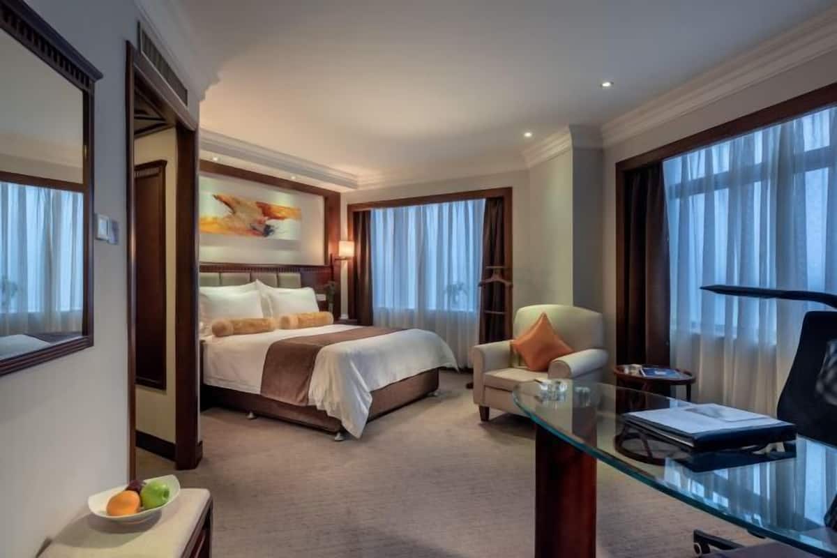 A hotel room with a bed, a desk, a chair, a glass table, and a large window.