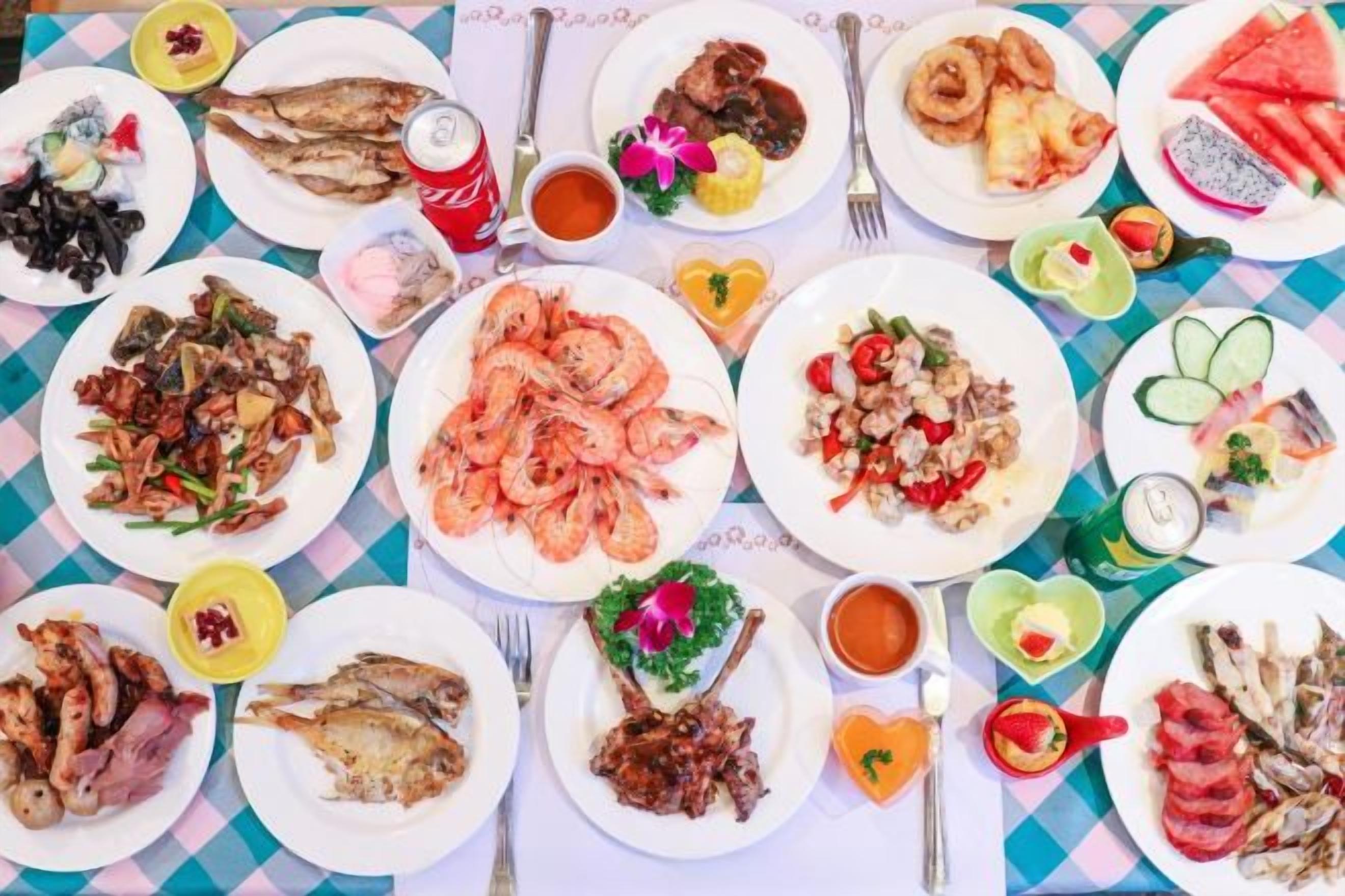 Une table où sont présentés divers plats de fruits de mer, notamment des crevettes et du poisson, disposés sur une nappe à carreaux.