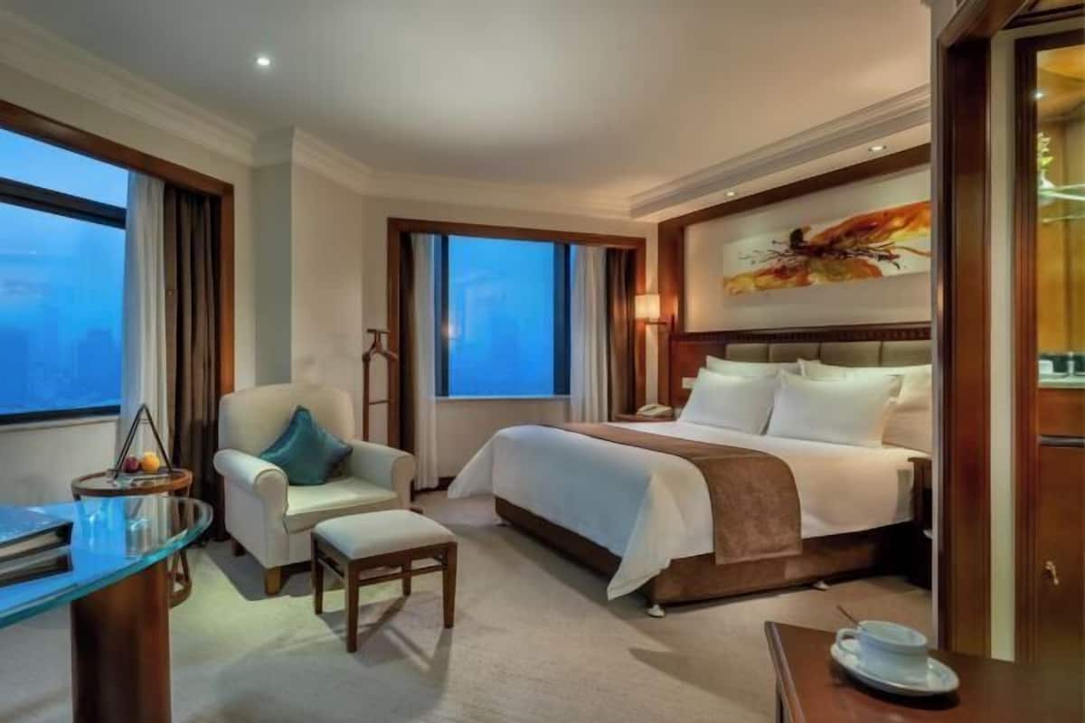 A hotel room with a bed, a desk, a chair, and a view of the city.