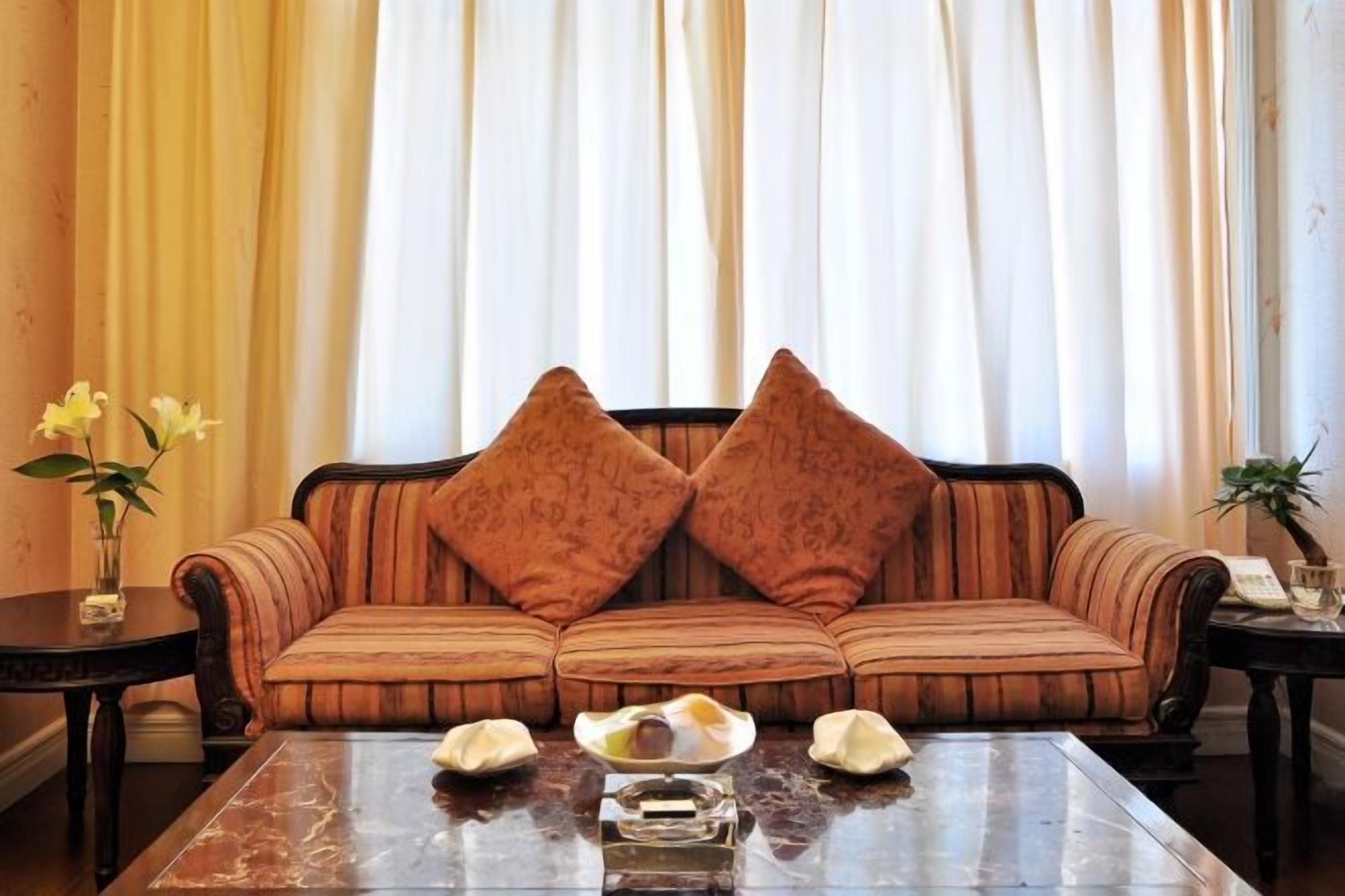 Un sofá con dos almohadones decorativos, una mesa de centro de vidrio con un florero y un cuenco, y una planta sobre una mesita auxiliar.