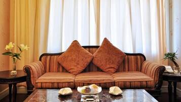 Un sofá con dos almohadones decorativos, una mesa de centro de vidrio con un florero y un cuenco, y una planta sobre una mesita auxiliar.