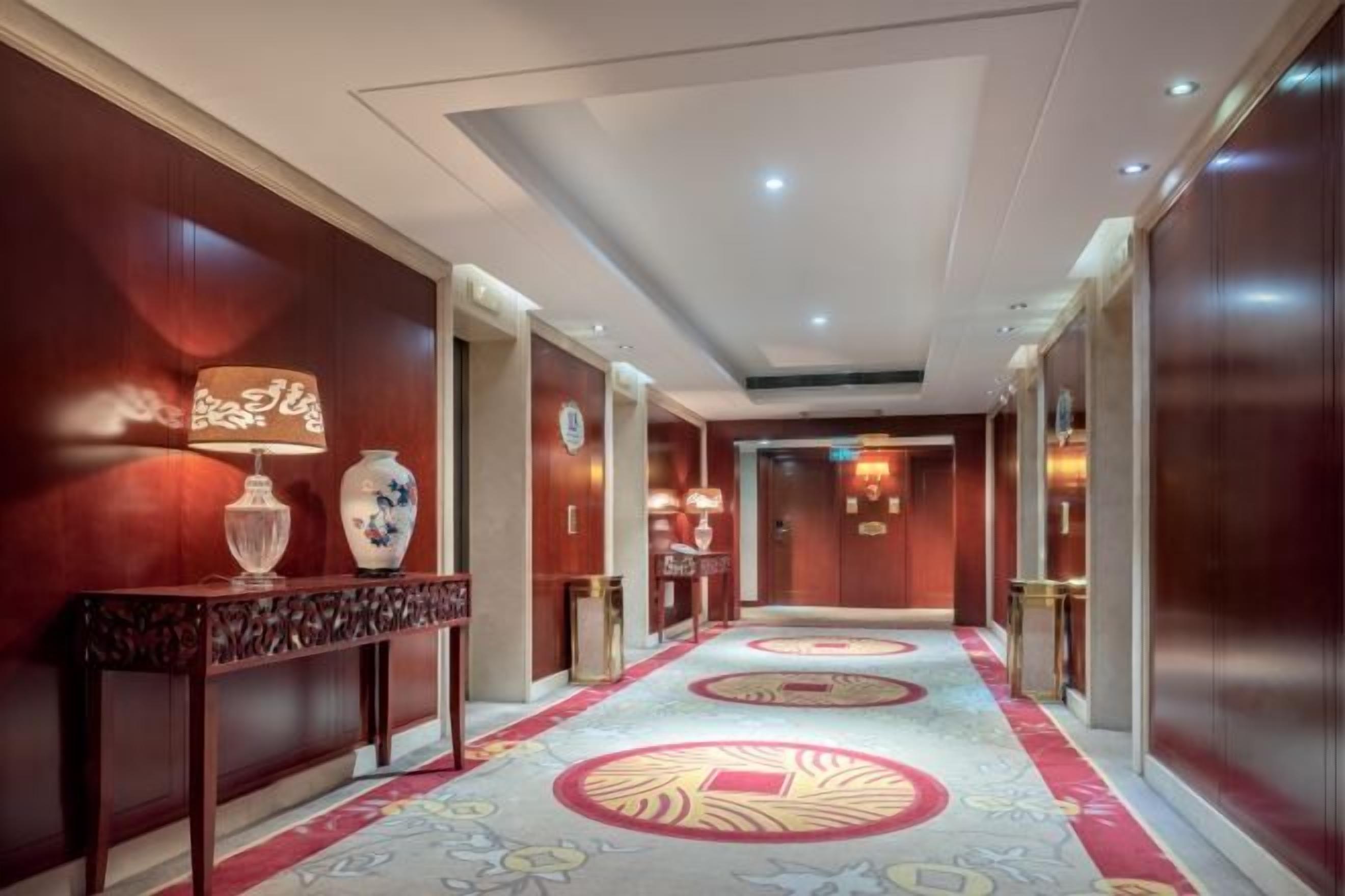 A hotel corridor with wooden walls, a patterned carpet, and a reception desk with a vase and lamp.