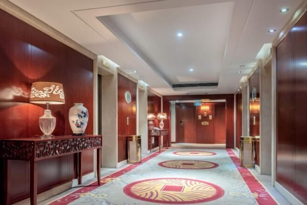 A hotel hallway with wooden paneling, a patterned carpet, and a reception desk with a vase and lamp.
