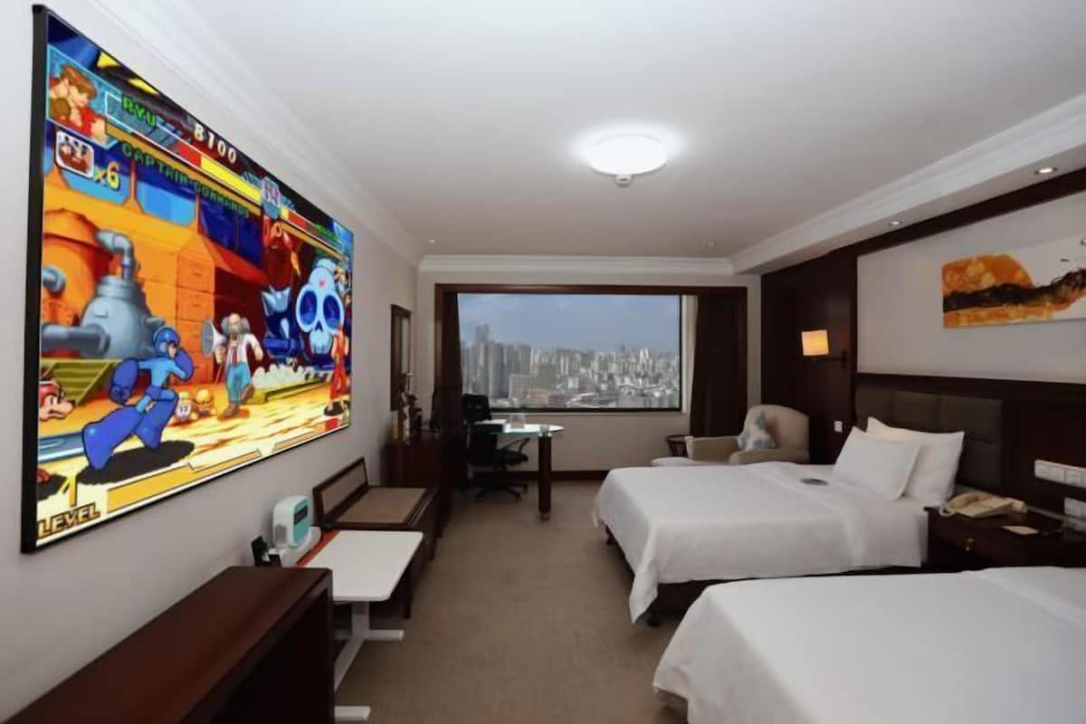 A hotel room with two beds, a desk, a chair, a TV, and a view of the city.