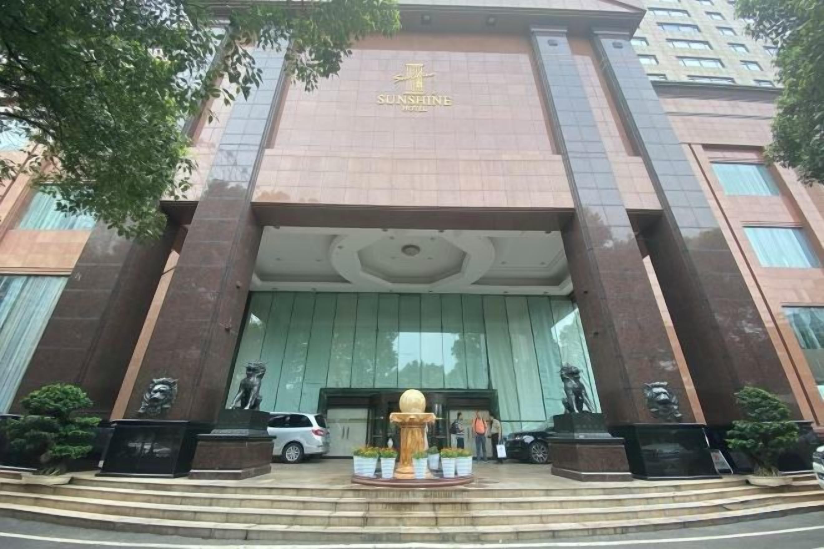 L’entrée d’un hôtel, avec un grand élément décoratif doré, une voiture garée devant et une statue sur la droite.