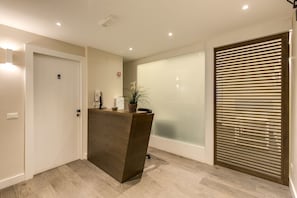 A reception desk with a plant, a fire extinguisher, and a door with a number sign. - Wrh Suites (Rome)