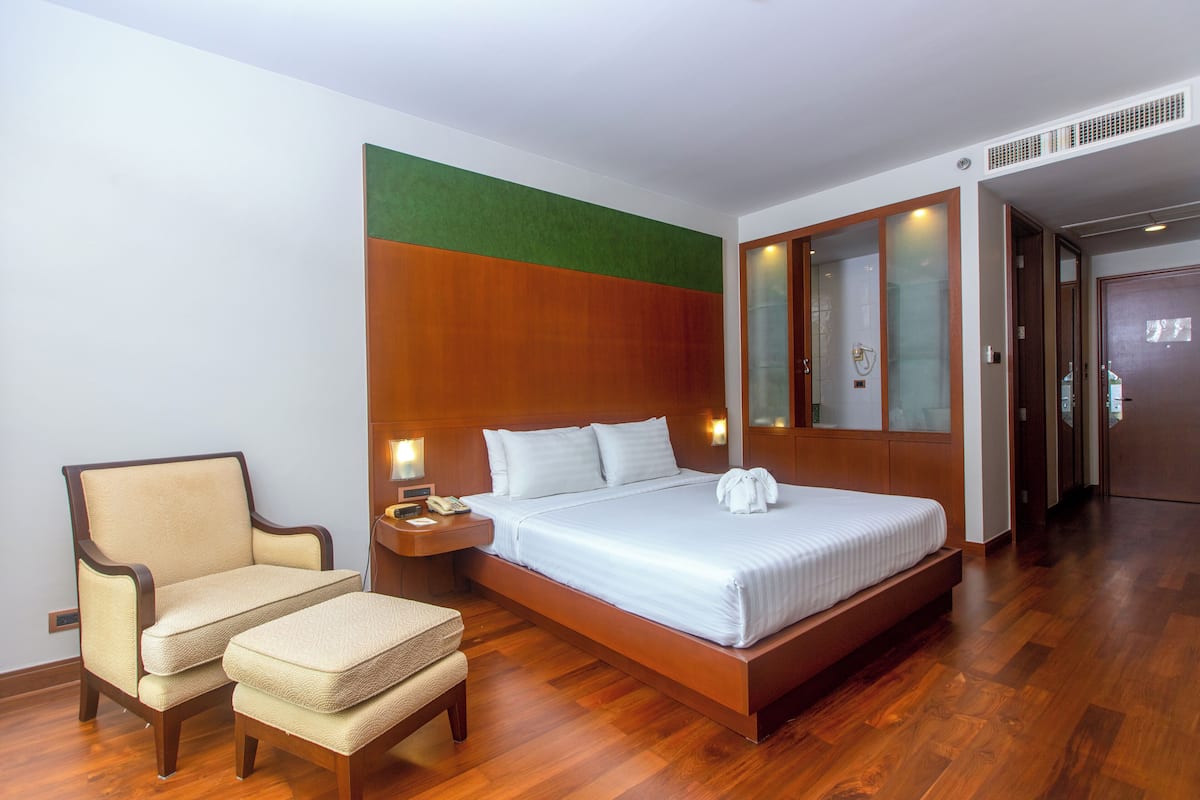 A hotel room with a large bed, a chair, a nightstand, and a mirror.
