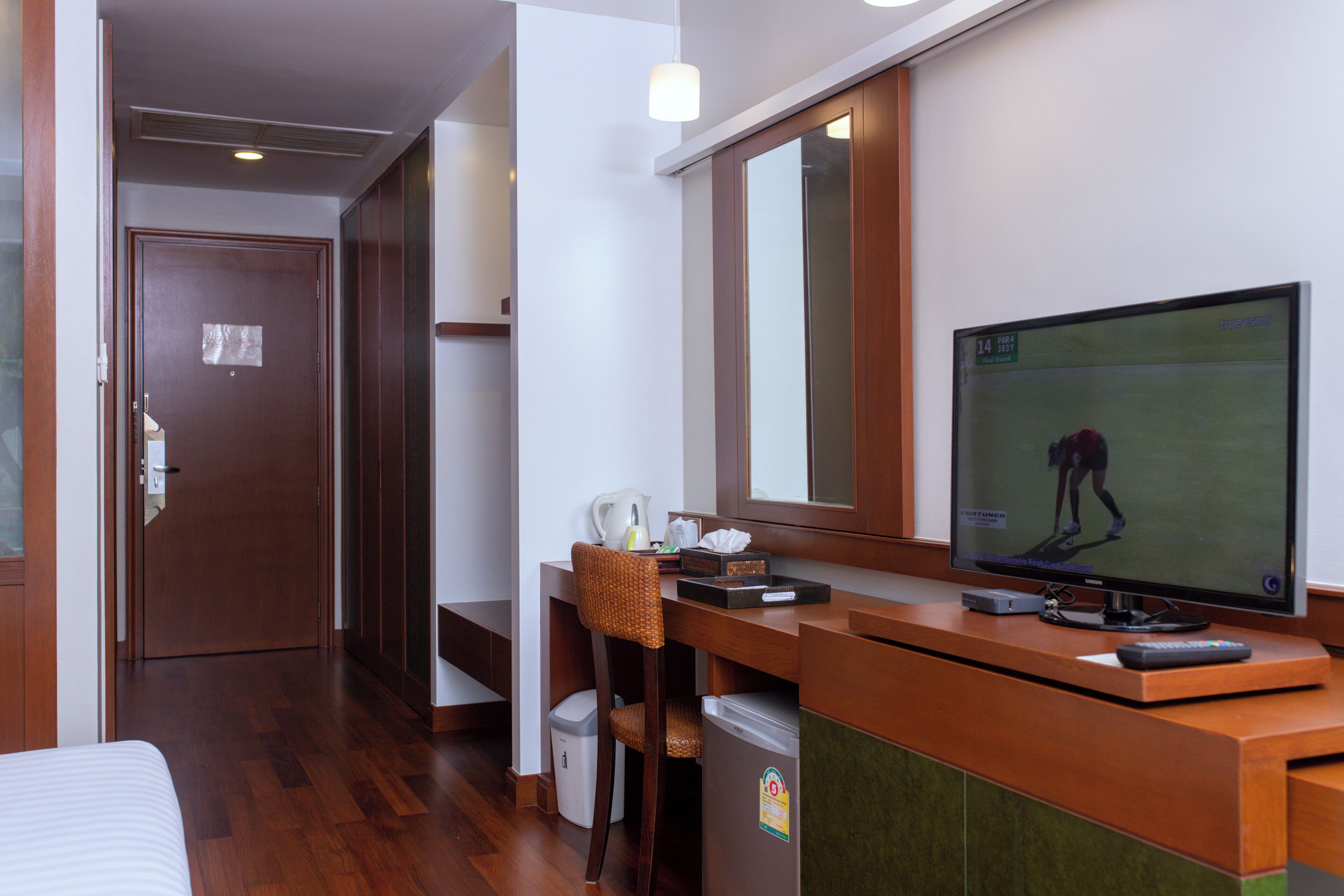 Habitación de hotel con un escritorio de madera, televisión, silla, un cubo de basura pequeño y una cama.