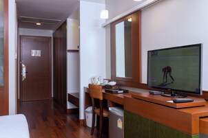 Habitación de hotel con un escritorio de madera, televisión, silla, un cubo de basura pequeño y una cama.