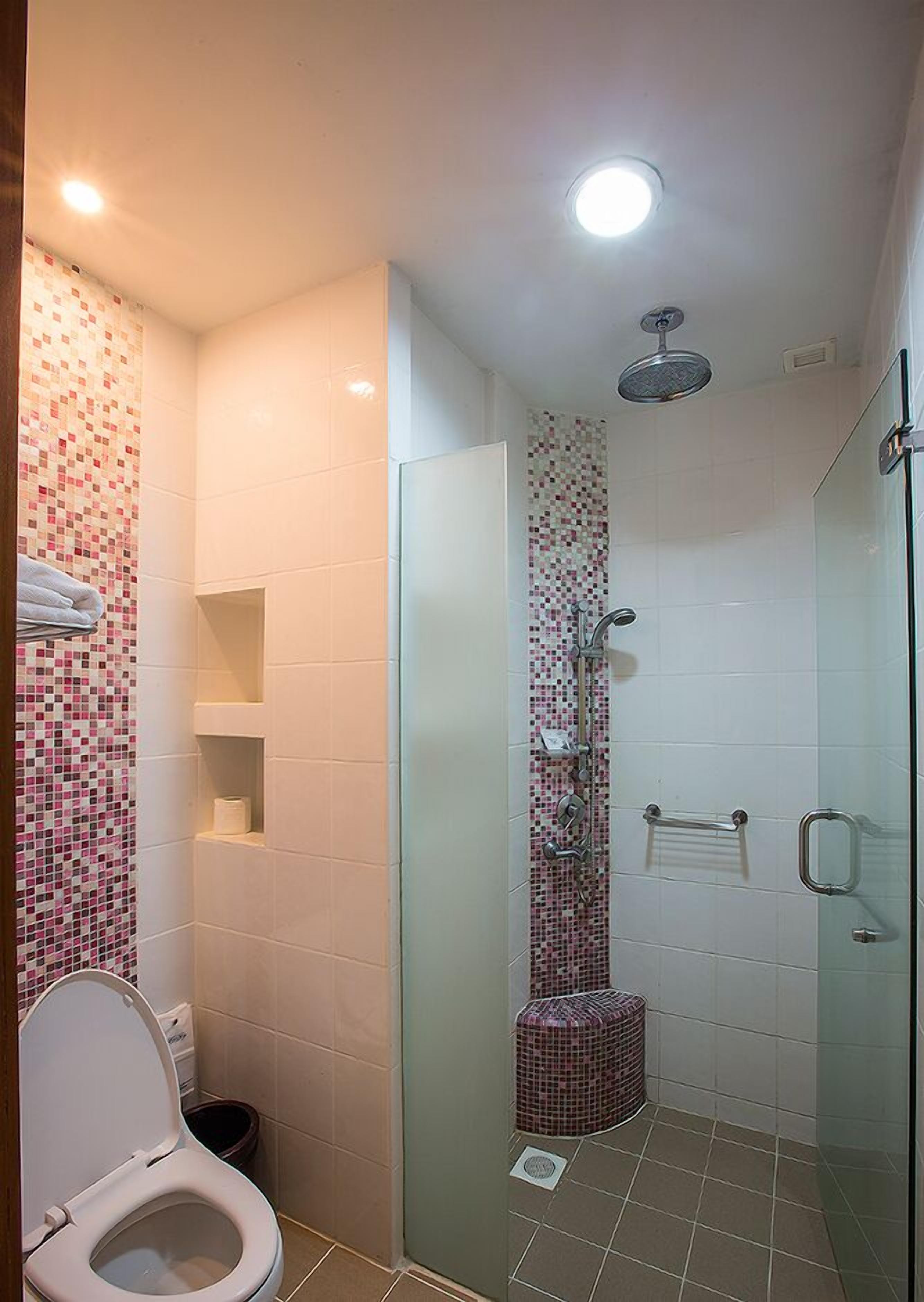 Un baño con cabina de ducha de vidrio, inodoro y una pequeña estantería con un rollo de papel higiénico.