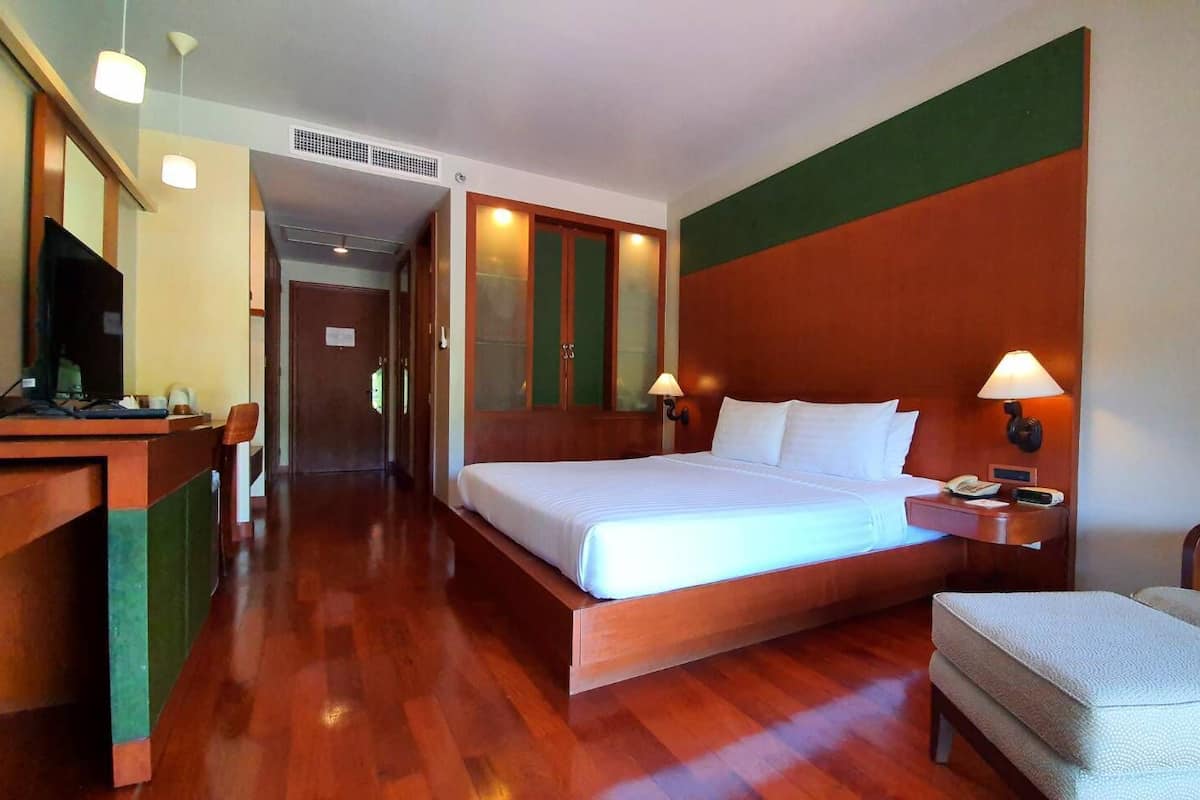 A hotel room with a bed, bedside table, chair, desk, and television.