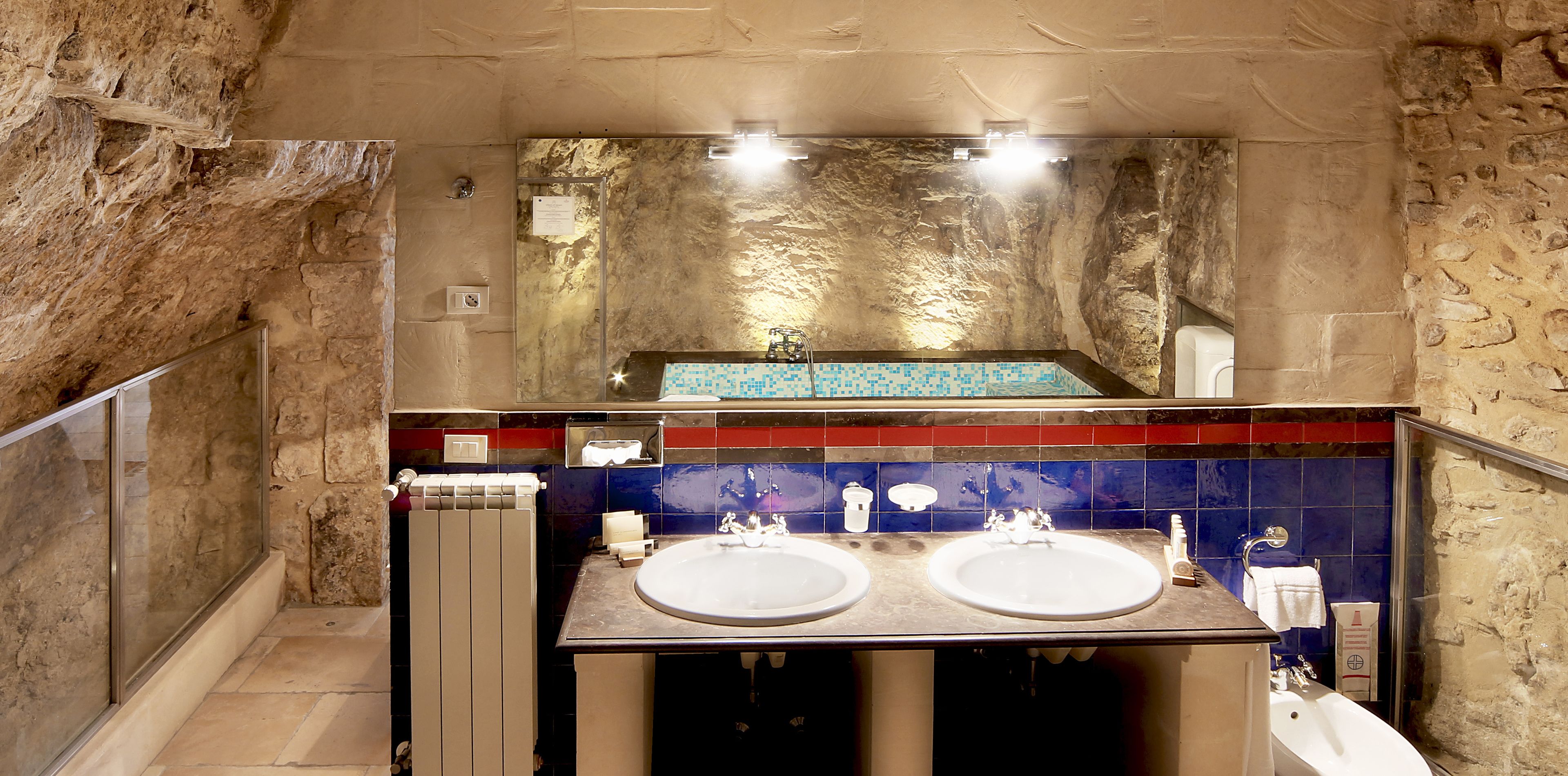 A bathroom with two sinks, a large mirror, and a stone wall.
