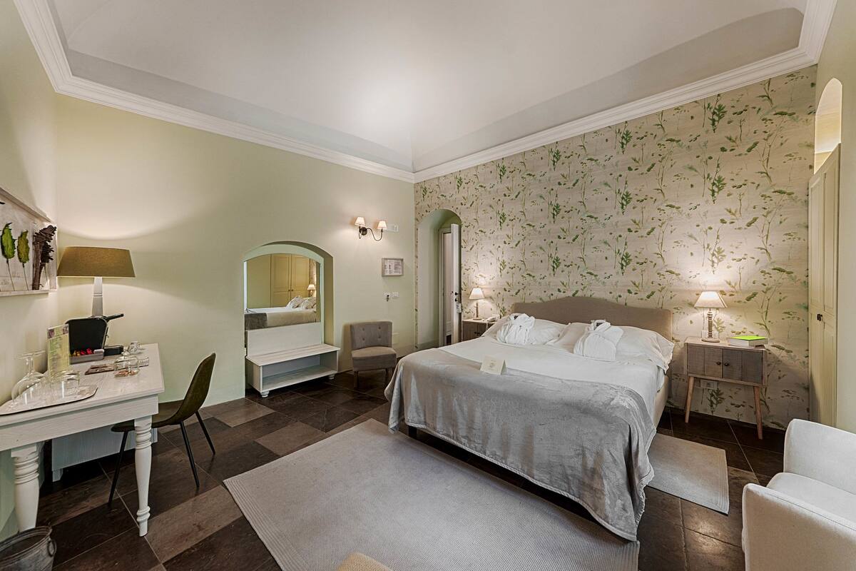 Ein Hotelzimmer mit Bett, Nachttischen, Schreibtisch mit Stuhl, Spiegel und Essbereich.