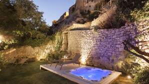Ein Whirlpool in einem Garten mit Steinmauern und Liegestühlen.