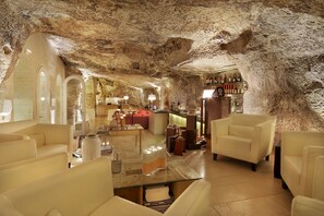 A spacious interior with a high ceiling, stone walls, and modern furnishings including leather sofas and a glass coffee table. - Locanda Don Serafino Historical Boutique Hotel (Ragusa)