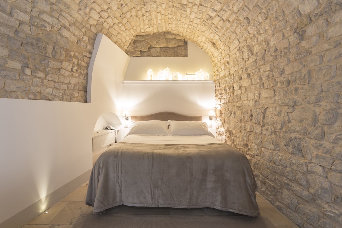 Ein Schlafzimmer mit einem steinernen Bogen, einem Bett mit Holz-Kopfstück und Wandleuchten.