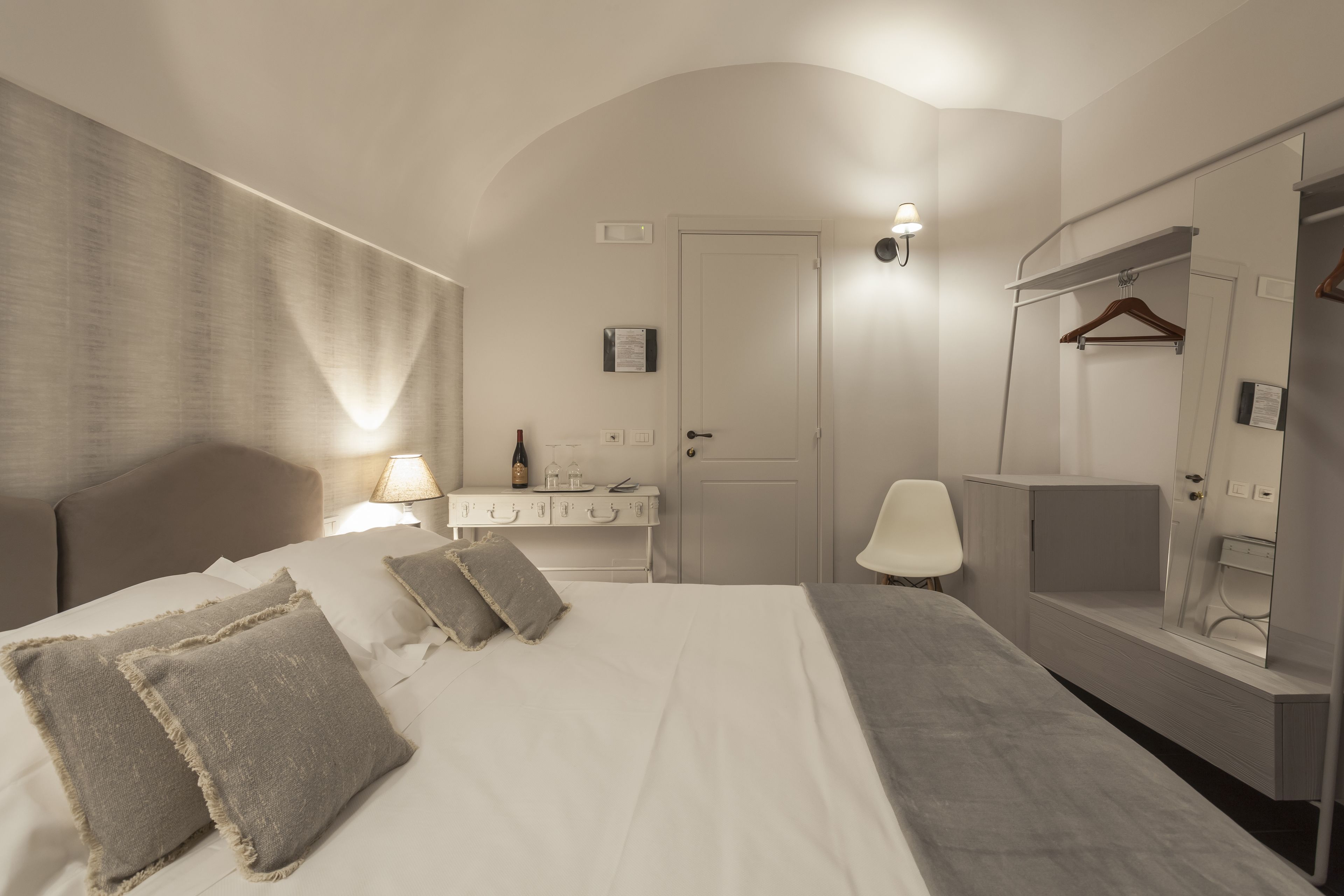 Een hotelkamer met een bed, nachtkastje, lamp en een spiegel.